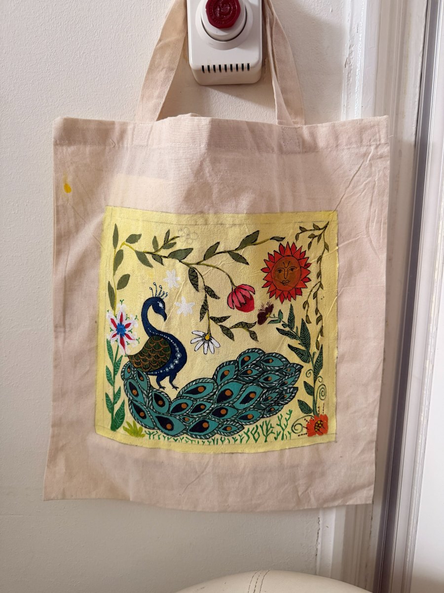 A cotton tote bag painted with a Madhubani peacock, sun and vines
