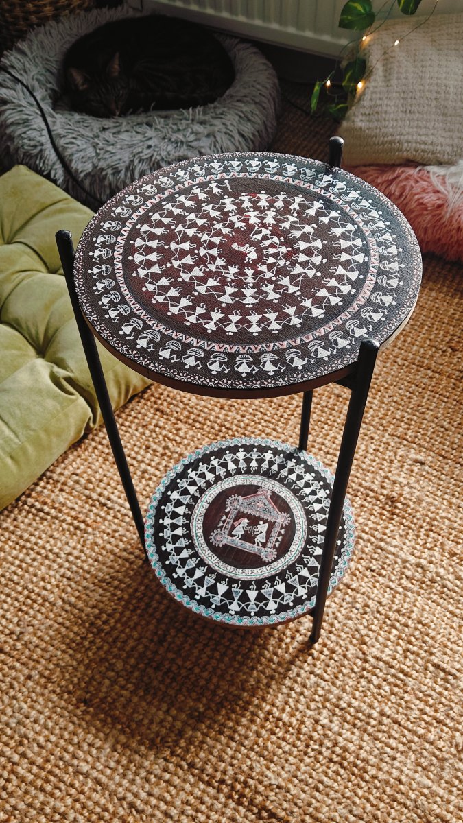 A two-tier side table painted with rings of white Warli figures
